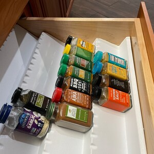 May include: A white drawer organizer with a variety of spice jars, including garlic, bay leaves, citrusy garlic, seasoning salt, and BBQ 101. The jars are arranged in rows and are mostly glass with colorful labels.