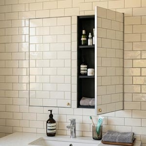 May include: A bathroom with white subway tile walls and a built-in medicine cabinet with a mirrored door. The cabinet is open, revealing shelves with toiletries. A sink, faucet, and accessories are in the foreground.