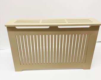 May include: A beige wooden radiator cover with a slatted top and vertical slats on the front. The cover has a simple, modern design.
