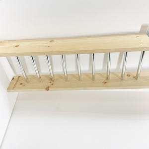 May include: A wooden shelf with a row of silver metal rods attached to the bottom. The shelf is mounted to a wall.