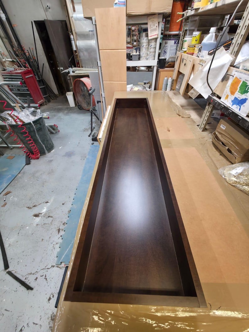May include: A rectangular, dark brown wooden box with a recessed interior. The box is open at the top and appears to be part of a larger woodworking project, possibly a cabinet or drawer. The wood has a polished finish.