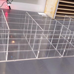 May include: Clear acrylic organizer with multiple compartments. The organizer has a rectangular shape with a series of vertical and horizontal dividers, creating numerous small cubicles. The design is transparent, allowing visibility of the contents.
