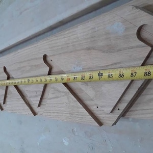 May include: A wooden coat rack with a series of cut-out shapes for hanging items. A yellow tape measure is laid across the rack, showing measurements in inches. The rack is made of light-colored wood.