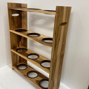 May include: A wooden plant stand with multiple circular openings for pots. The stand has a natural wood grain finish and a rectangular shape with several shelves. The openings are lined with black rings.