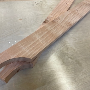 May include: Two pieces of unfinished, light brown wood with rounded edges. The wood is stacked on top of each other.