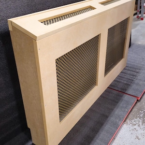 May include: A light brown wooden radiator cover with two rectangular openings covered with a metal mesh grille. The cover is angled to the right.