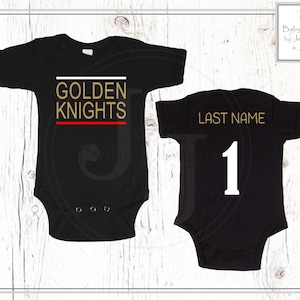May include: Black baby bodysuit with "GOLDEN KNIGHTS" in gold lettering, with a white and red stripe design. The back of the bodysuit has "LAST NAME" in gold and the number "1" in white.