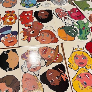 May include: A set of colorful illustrated character faces, printed on white cardstock. The faces are of various people, animals, and cartoon characters. The characters are all smiling and have different expressions.