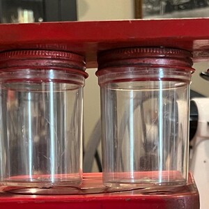 May include: A red wooden spice rack with six clear glass jars with red lids. The jars are empty and ready to be filled with spices.