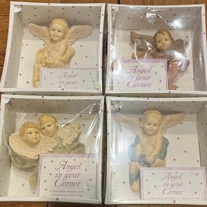 May include: Four boxed angel figurines. Each angel is in a different pose, with wings and a serene expression. The boxes have a decorative star pattern and a label that reads "Angel in your Corner".
