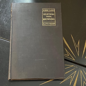 May include: A dark gray book titled "Selections from Browning" with gold lettering. The book is part of the "Academy Classics" series and published by Allyn and Bacon. The book is on a dark surface.