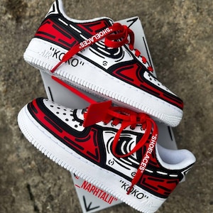 May include: A pair of low-top sneakers featuring a comic-book style graphic design in red, black, and white. The shoes have red laces printed with the word SHOELACES, a red zip tie, and the text KOKO and NAPHTALI printed on the white midsoles.