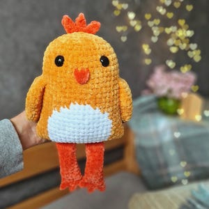 May include: A crocheted plush toy chick with orange and white yarn. The chick has a red comb and black eyes.
