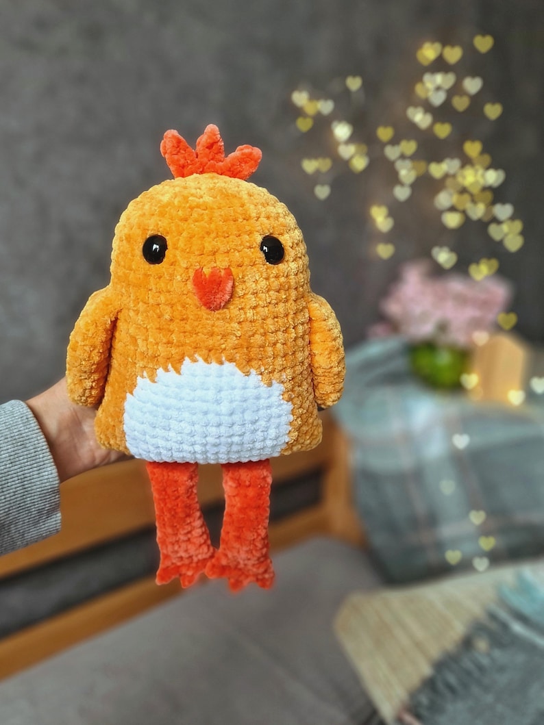 May include: A crocheted plush toy chick with orange and white yarn. The chick has a red comb and black eyes.