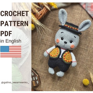 Könnte beinhalten: Häkelanleitung PDF in Englisch für einen grauen Hasen, der einen schwarzen Hut mit bunten Verzierungen und eine gelbe und orangefarbene Weste trägt. Der Hase liegt auf einer braunen Jutestoffoberfläche.