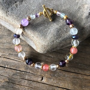 Puede incluir: Un brazalete de tono dorado con cierre de palanca que presenta cuentas transparentes, amatista, cuarzo rosa y fluorita.