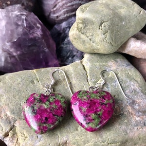 May include: A pair of heart-shaped earrings featuring a green and pink gemstone. The earrings are made from sterling silver and have a hook fastening.
