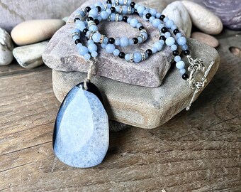 May include: A light blue agate pendant necklace with black and silver beads. The pendant is a teardrop shape with a black border and a white center.