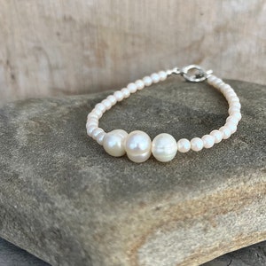 May include: A white pearl bracelet with three larger pearls in the centre.