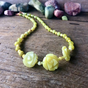 May include: A green jade necklace with carved flower beads. The necklace is made of small, round beads and features three larger beads that are carved into the shape of roses.