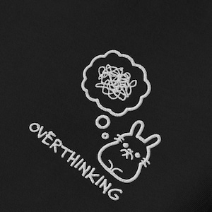 Puede incluir: Parche bordado negro con un contorno blanco de un conejo con una burbuja de pensamiento sobre su cabeza. La burbuja de pensamiento está llena de un garabato. El texto "OVERTHINKING" está escrito en diagonal debajo del conejo.