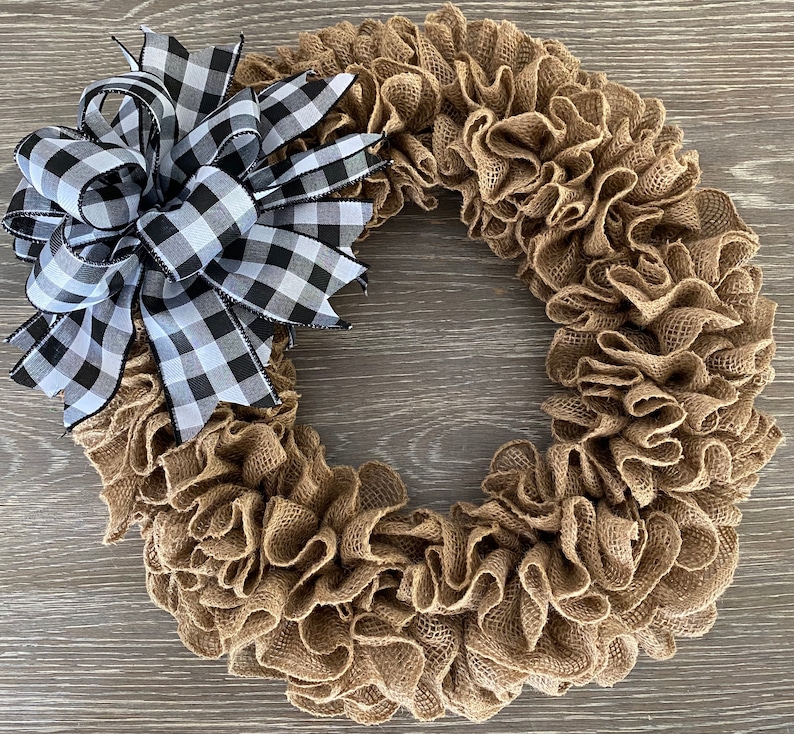 May include: A brown burlap wreath with a black and white checkered bow. The wreath is made of burlap fabric that has been gathered and ruffled to create a full and fluffy look. The bow is tied at the top of the wreath and is made of a black and white checkered ribbon.