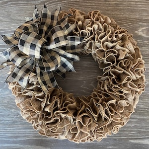 May include: A brown burlap wreath with a black and white checkered bow. The wreath is made of burlap ruffles and is perfect for a farmhouse or rustic decor style.