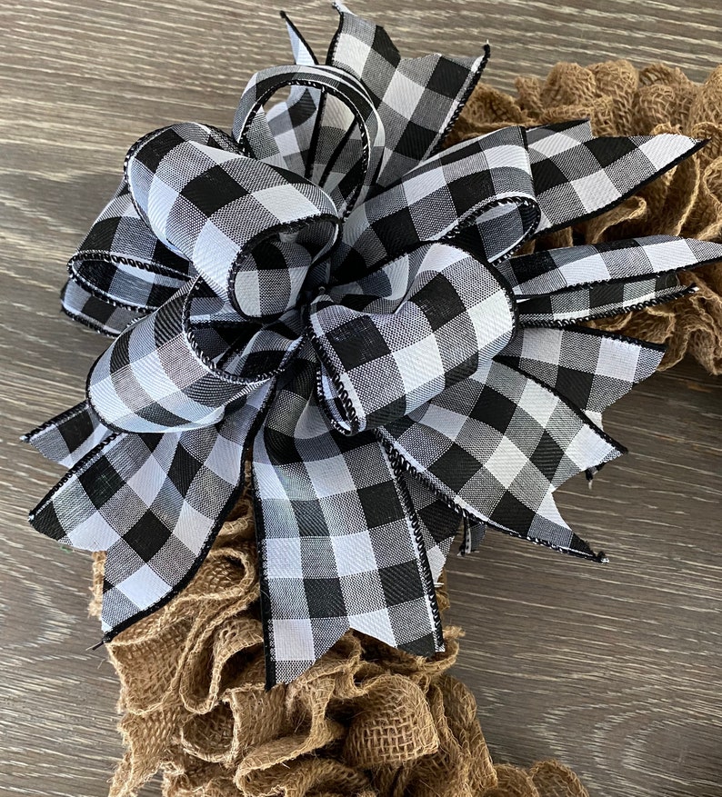 May include: A black and white checkered bow with black trim, tied on a brown burlap wreath.