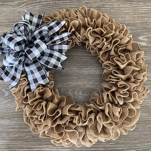 May include: A brown burlap wreath with a black and white checkered bow. The wreath is made of burlap ruffles and is perfect for a farmhouse or rustic decor style.