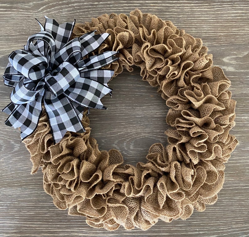 May include: A brown burlap wreath with a black and white checkered bow. The wreath is made of burlap ruffles and is perfect for a farmhouse or rustic decor style.