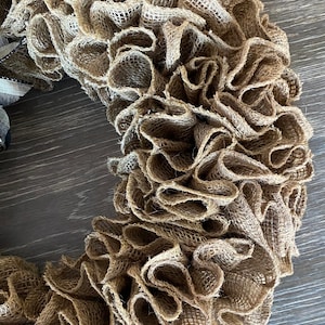 May include: A brown burlap wreath with a ruffled texture. The wreath is made of burlap fabric and has a natural, rustic look.
