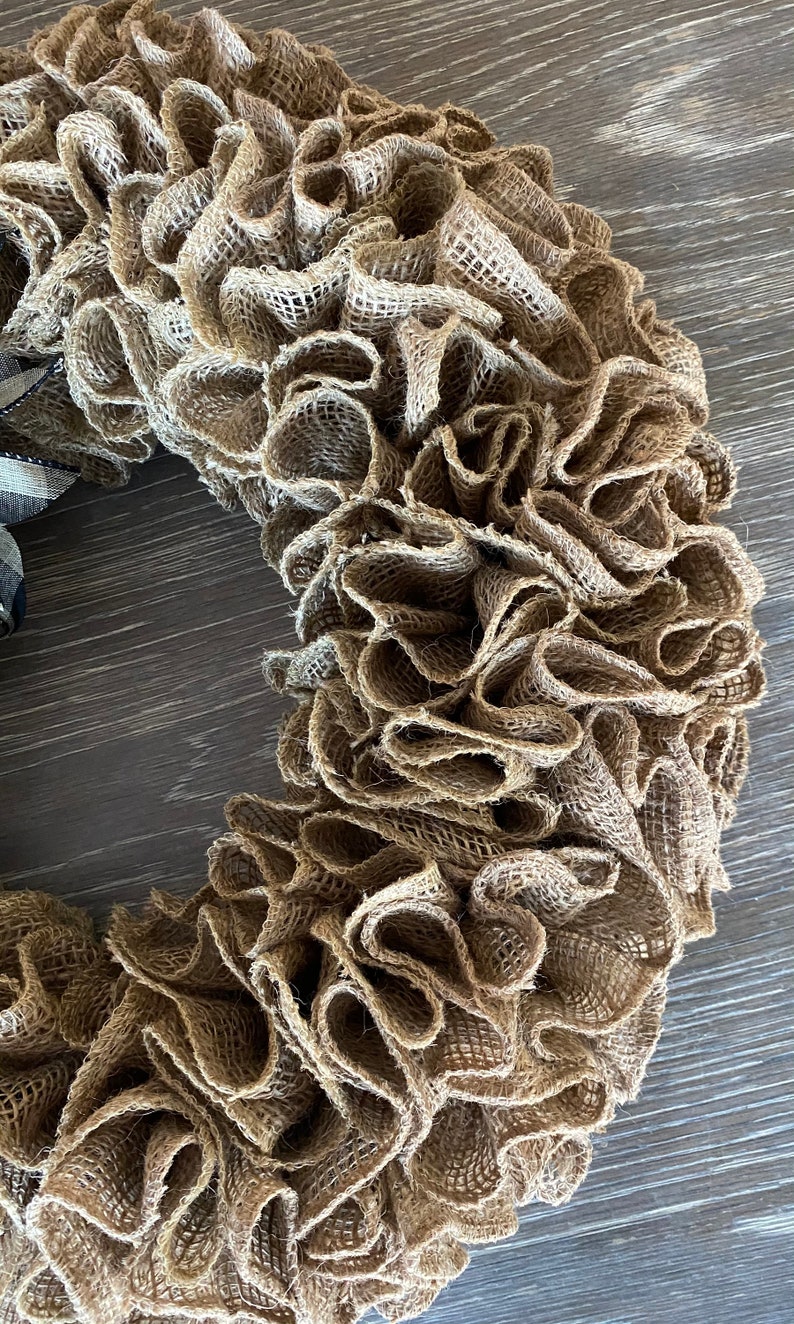 May include: A brown burlap wreath with a ruffled texture. The wreath is made of burlap fabric and has a natural, rustic look.