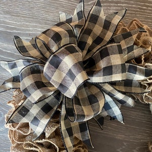 May include: A black and tan checkered ribbon bow with black trim, tied on a burlap wreath.