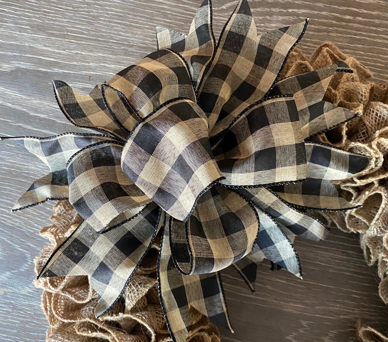 May include: A black and tan checkered ribbon bow with black trim, tied on a burlap wreath.