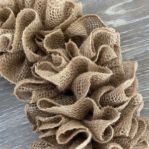 May include: A brown burlap wreath with a ruffled texture. The wreath is made of natural fibers and has a rustic look.