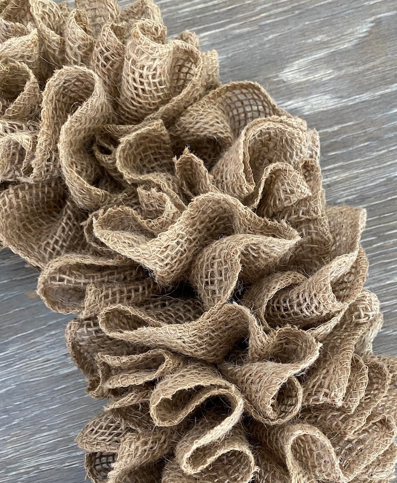 May include: A brown burlap wreath with a ruffled texture. The wreath is made of natural fibers and has a rustic look.
