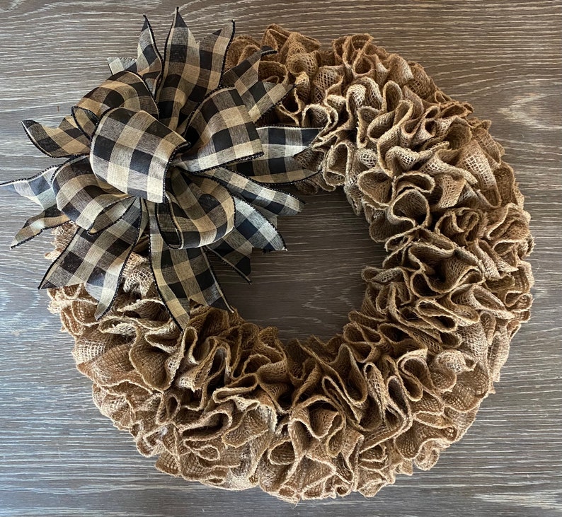 May include: A brown burlap wreath with a black and white checkered bow. The wreath is made of burlap and has a ruffled texture. The bow is tied in a knot and has a long tail.