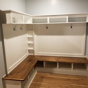 May include: White corner bench with a wooden top and shelves. The bench has hooks for hanging coats or bags.