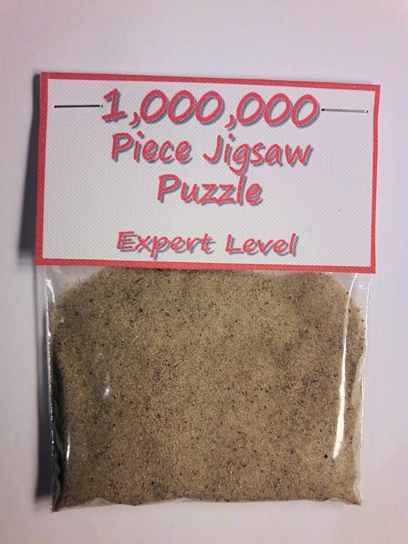 May include: A clear plastic bag filled with a tan substance, labeled with a red-bordered sign that reads "1,000,000 Piece Jigsaw Puzzle" and "Expert Level" in red text. The bag is sealed at the top.