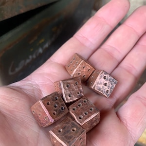 May include: Six copper dice with a hammered texture. Each die has a different number of dots on each side.
