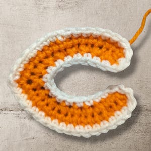 May include: A crocheted letter C in orange and white yarn. The letter is made with a single crochet stitch and has a white border.