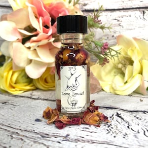 May include: A small glass bottle with a black cap filled with a clear liquid and dried rose petals. The label reads "No. 3 Love Bound New Moon Vibes".