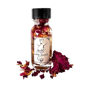 May include: A small glass bottle filled with a clear liquid and rose petals. The bottle has a black cap and a label that reads "No. 3 Love Bound New Moon Vibes".