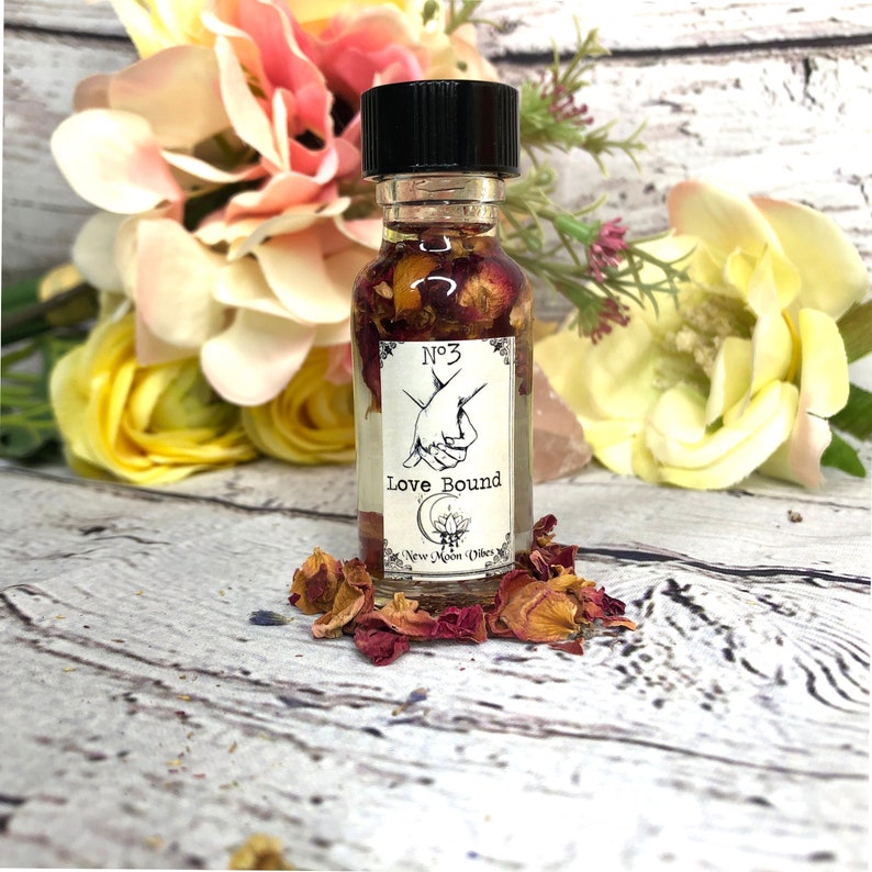 K&ouml;nnte beinhalten: Eine kleine Glasflasche mit schwarzem Verschluss, gef&uuml;llt mit einer klaren Fl&uuml;ssigkeit und getrockneten Rosenbl&uuml;ten. Das Etikett lautet "No. 3 Love Bound New Moon Vibes".