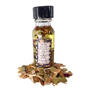 May include: A small glass bottle with a black cap filled with a yellow oil and herbs. The label reads "No.40 Success Affirmation Oil" with a pentagram symbol. The bottle is sitting on a pile of dried herbs and wood chips.