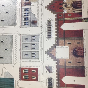 May include: A paper model kit of a medieval castle with detailed instructions and numbered pieces. The castle has a red roof, gray walls, and a large arched doorway.