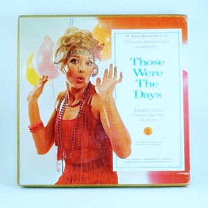 Puede incluir: Una portada de álbum de vinilo vintage con una mujer con un vestido rojo de flapper y una expresión de sorpresa. El título del álbum es "Those Were The Days" y el texto "A delightful collection of memory tunes from a dazzling era" está impreso debajo del título.