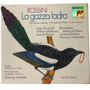 Puede incluir: Una portada de álbum de vinilo vintage con una urraca en blanco y negro con un anillo dorado en su pico. El álbum es para la ópera La gazza ladra de Rossini, con el título en letras grandes y en negrita. El álbum presenta los nombres de los intérpretes, incluyendo Katia Ricciarelli, William Matteuzzi y Samuel Ramey. El álbum es una grabación en vivo.