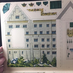 May include: A vintage paper model kit of a castle with detailed illustrations of the building's exterior, including windows, doors, and a roof. The kit includes numbered pieces that can be cut out and assembled to create a three-dimensional model.