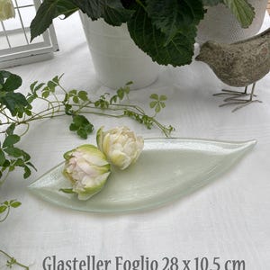 K&ouml;nnte beinhalten: Eine blattf&ouml;rmige, hellgr&uuml;ne Glasservierschale mit zwei wei&szlig;en und rosa Tulpen. Die Schale ist 28 cm lang und 10,5 cm breit. Der Text "Glasteller Foglio 28 x 10,5 cm" ist auf der wei&szlig;en Oberfl&auml;che aufgedruckt.